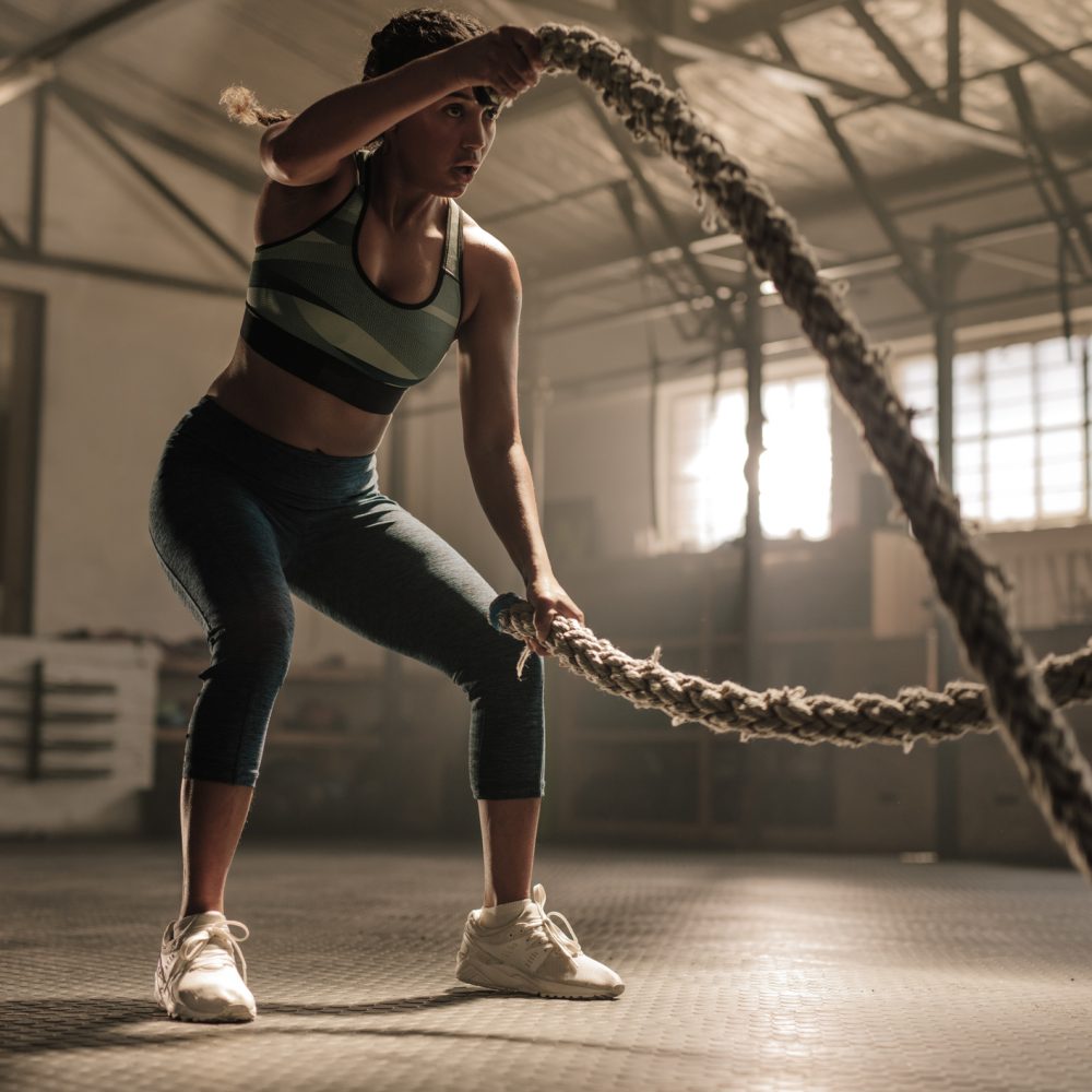 Fitness woman using training ropes for exercise at gym. Athlete working out with battle ropes at cross gym.